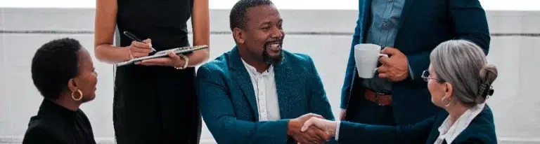 A man shakes hands with a salesperson after a successful sales meeting as his colleagues look on