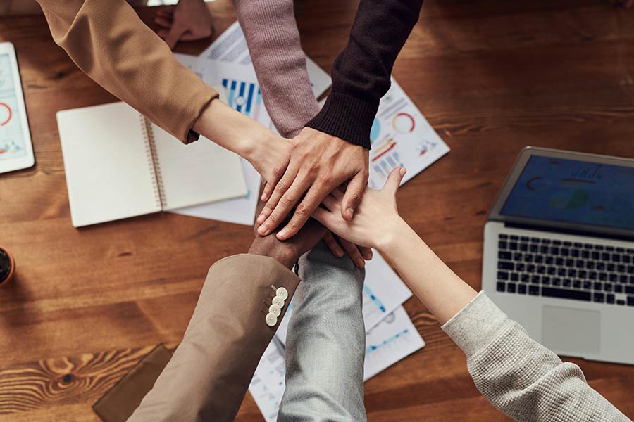 A sales team places their hands together over a desk in a sign of teamwork