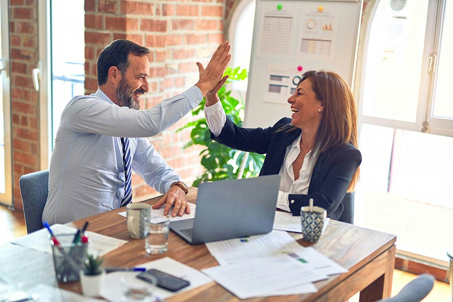 Two sales account executives high-five each other in an office setting after closing a deal