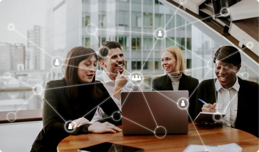 Four business professionals in a modern office sitting around a table, collaborating during a meeting; one taking notes, another using a laptop, with digital network icons overlaid symbolizing connectivity and teamwork.