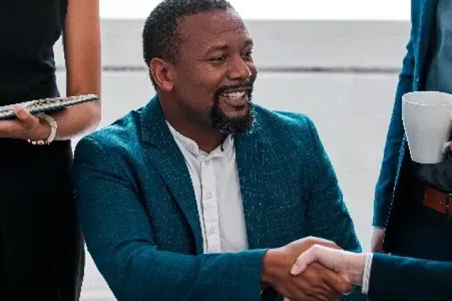 A man shakes hands with a salesperson after a successful sales meeting as his colleagues look on